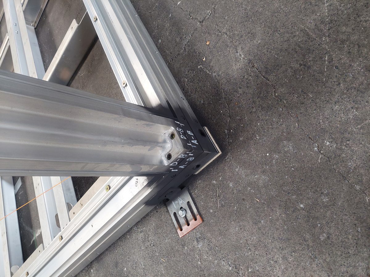 Base corner of Anyplace frame with removable screw-pile foundation plate visible — A-B and D-B markings show position-tracked installation