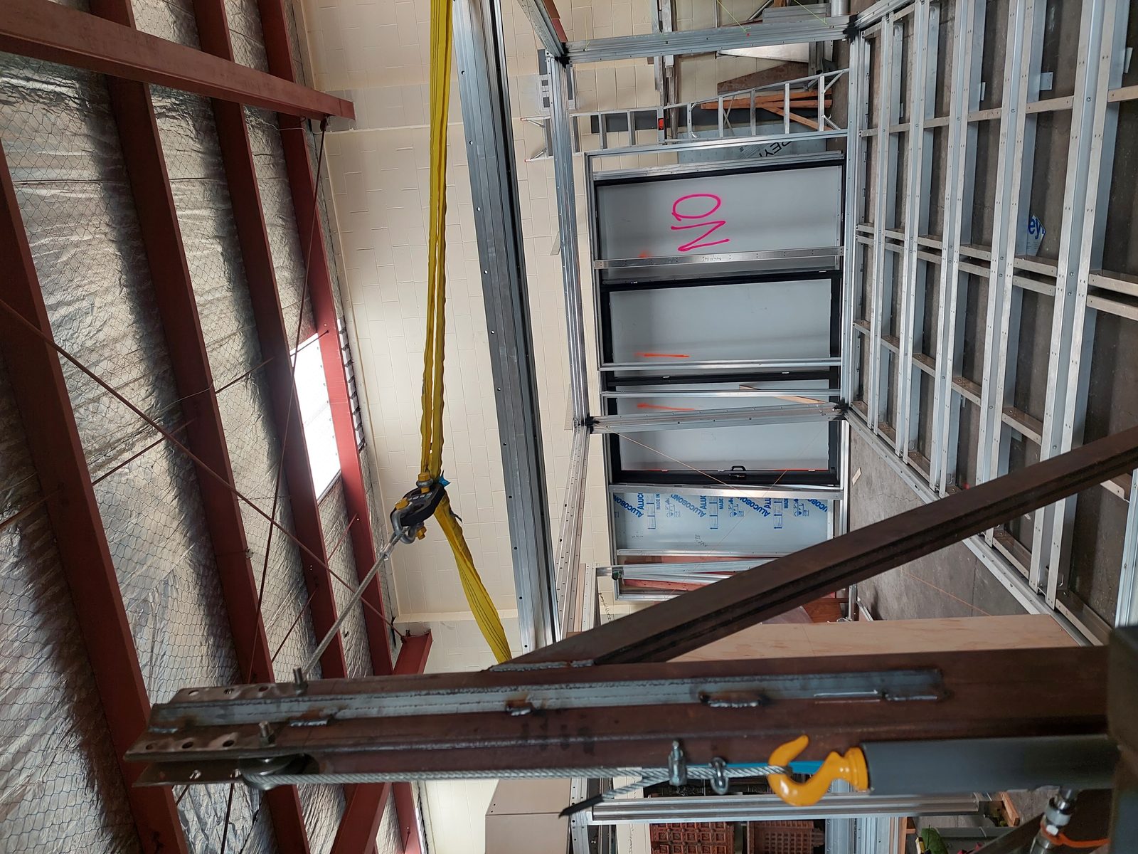 Anyplace module suspended under live load test, 2024 — yellow rigging strap visible from overhead structural beam, full module construction visible below